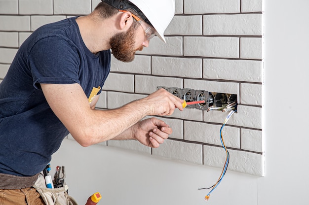 Trabalhador da construção civil eletricista com barba de macacão durante a instalação de tomadas. Conceito de renovação em casa.