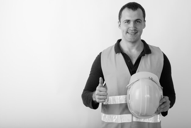 Trabalhador da construção civil feliz jovem homem musculoso sorrindo enquanto abre o polegar e segura o capacete