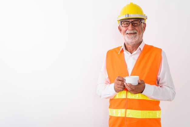 trabalhador da construção civil feliz sênior barbudo sorrindo e segurando a xícara de café enquanto usava óculos em branco