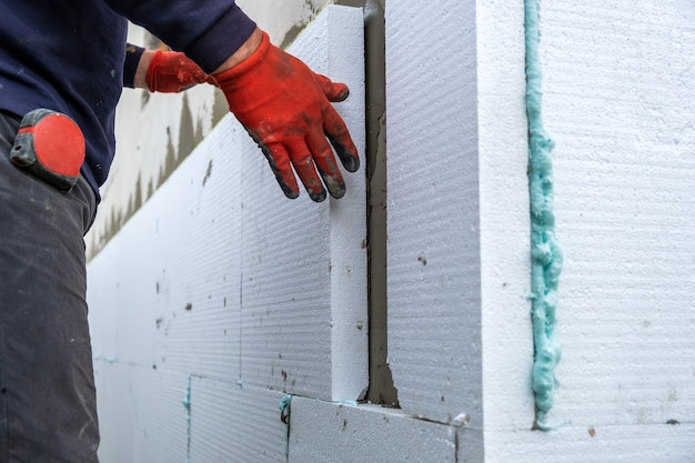Trabalhador da construção civil instalando folhas de isolamento de isopor na parede da fachada da casa para proteção térmica.