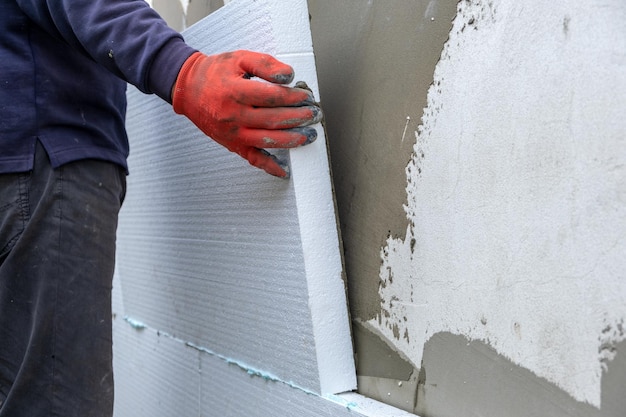 Trabalhador da construção civil instalando placas de isolamento de isopor na parede da fachada da casa para proteção térmica.