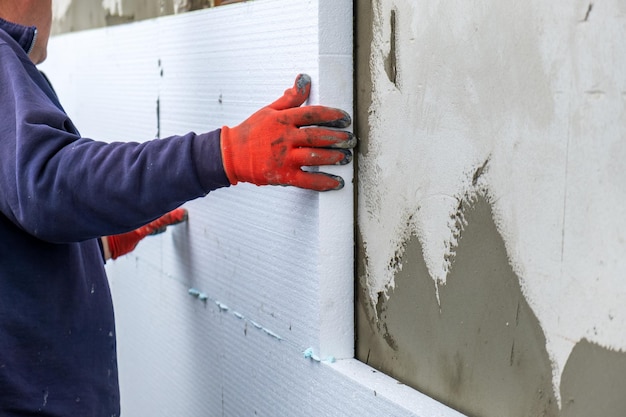 Trabalhador da construção civil instalando placas de isolamento de isopor na parede da fachada da casa para proteção térmica.