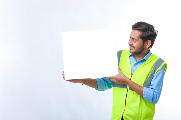 Trabalhador da construção civil jovem indiano apresentando placa de cartaz vazio sobre fundo branco.