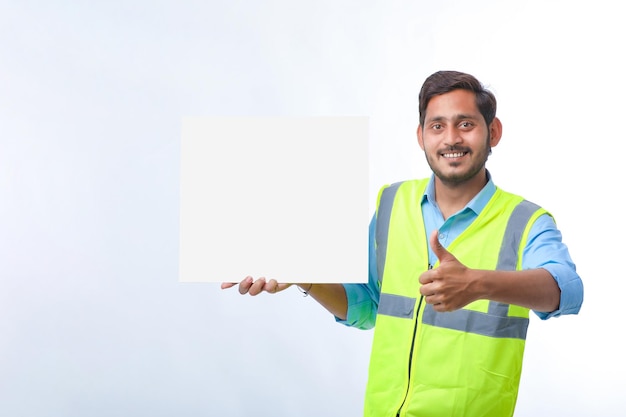 Trabalhador da construção civil jovem indiano apresentando placa de cartaz vazio sobre fundo branco.