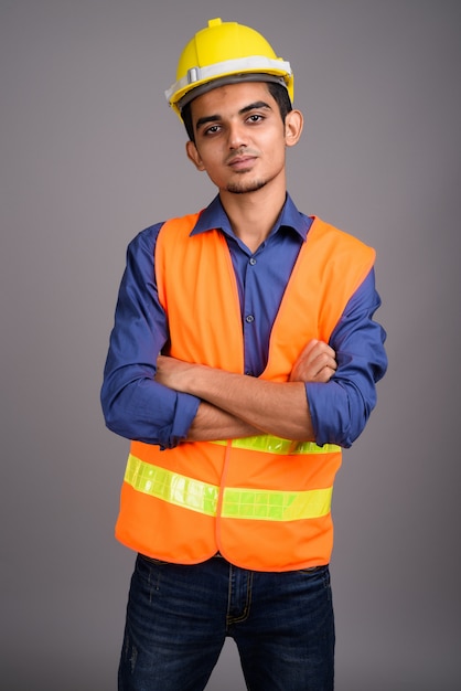 Trabalhador da construção civil jovem indiano contra parede cinza