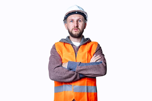 Trabalhador da construção civil masculino jovem no capacete com os braços cruzados sobre fundo claro.