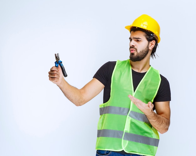 Trabalhador da construção civil segurando um alicate azul e parece confuso e insatisfeito.