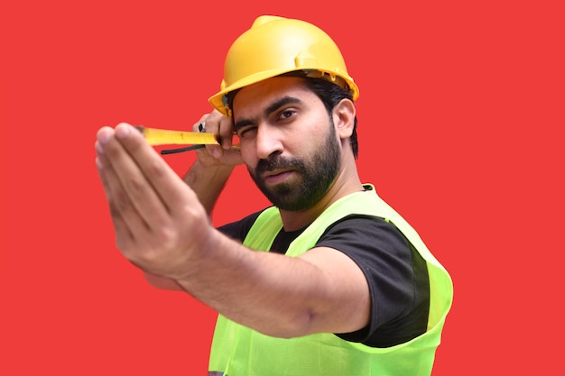 trabalhador da construção civil segurando uma fita métrica posando sobre fundo vermelho modelo indiano do paquistanês