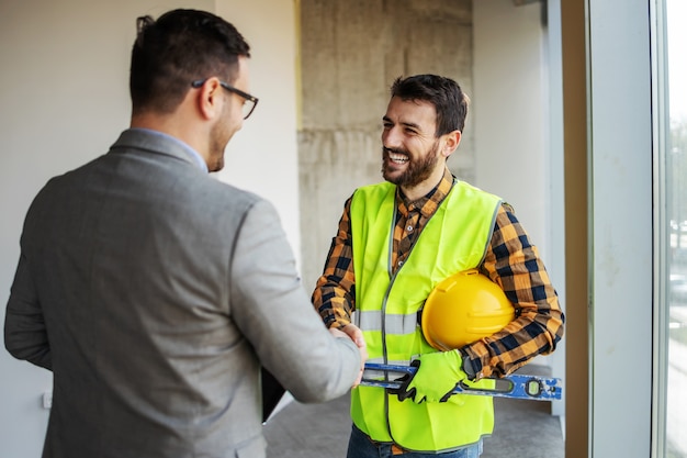 Trabalhador da construção civil sorridente, cumprimentando o supervisor em um edifício em processo de construção