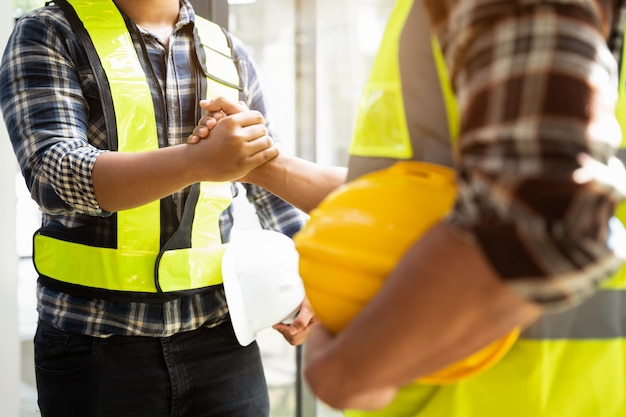 Foto trabalhador da construção civil usando capacete de proteção e colete está segurando a mão de seu colega enquanto trabalha