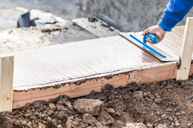 Trabalhador da construção civil usando espátula em cimento úmido formando um revestimento em torno de uma nova piscina