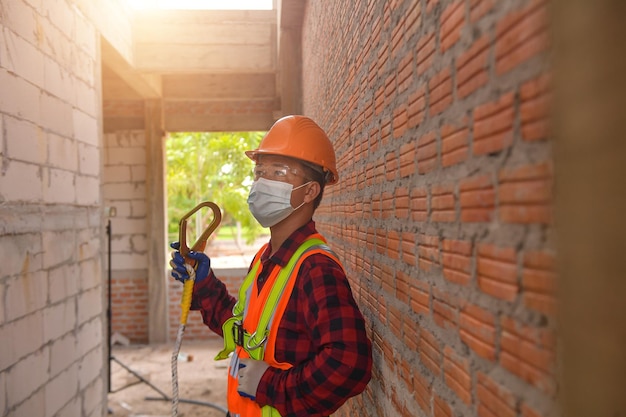 Trabalhador da construção civil usando trabalho de segurança em uniforme alto em andaimes no canteiro de obras durante o pôr do sol, trabalhando em equipamentos de altura.