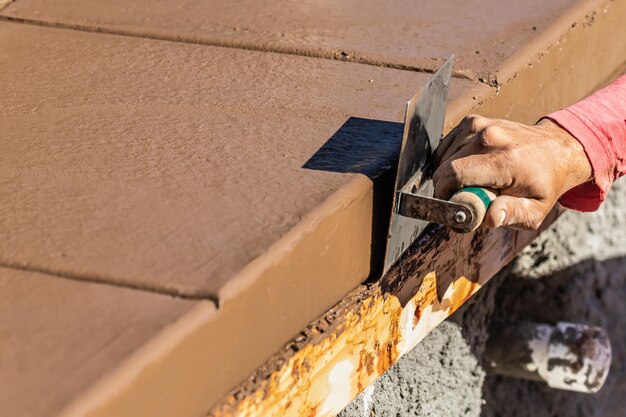 Trabalhador da construção usando uma faca de aço inoxidável na formação de cimento molhado ao redor de uma nova piscina