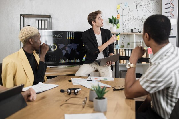 Trabalhador da empresa masculino com roupa formal sentado na mesa do escritório e ouvindo o líder da equipe