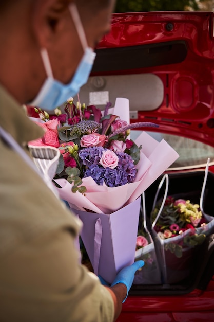 Trabalhador da floricultura baixando cuidadosamente um pacote de flores no porta-malas traseiro de um automóvel