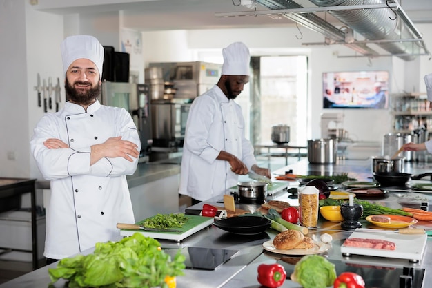 Trabalhador da indústria alimentar com habilidades de cozinha gourmet, preparando legumes e especiarias para uma refeição deliciosa. Sous chef vestindo uniforme de cozinha, em pé na cozinha profissional do restaurante, olhando para a câmera.