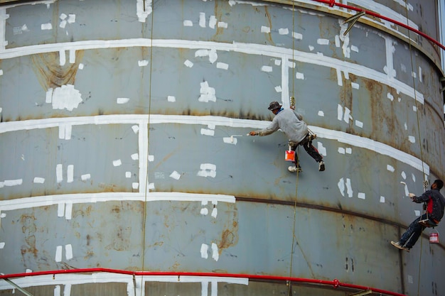 Trabalhador de acesso por corda industrial pendurado na placa de reservatório de óleo do tanque