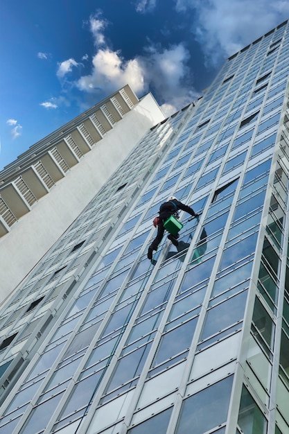 Trabalhador de alpinismo industrial lavando vidraças de fachadas externas paira sobre a construção de fachadas residenciais