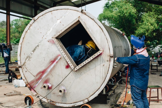 Trabalhador de argônio de soldagem macho reparado metal está soldando faíscas óleo de tanque de construção industrial fora