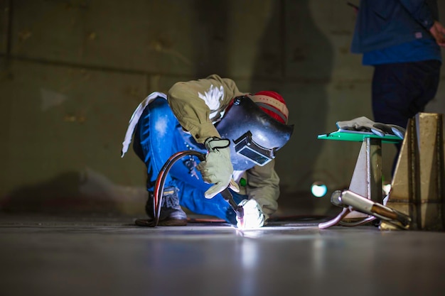 Trabalhador de argônio de soldagem macho reparado metal está soldando faíscas tanque de construção industrial óleo inoxidável dentro de espaços confinados