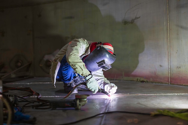 Trabalhador de argônio de soldagem macho reparado metal está soldando faíscas tanque de construção industrial óleo inoxidável dentro de espaços confinados