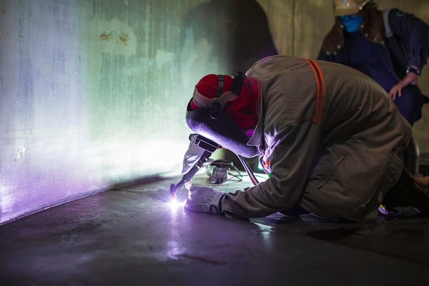 Trabalhador de argônio de soldagem macho reparado metal está soldando faíscas tanque de construção industrial óleo inoxidável dentro de espaços confinados