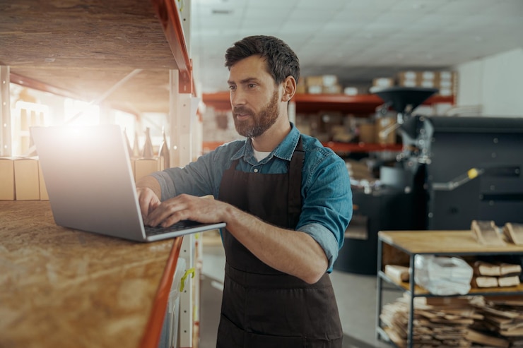 Foto trabalhador de armazém em uniforme de pé em uma pequena fábrica de café com laptop