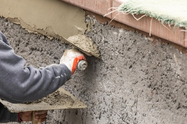 Trabalhador de azulejo aplicando cimento com espátula no canteiro de obras de piscina