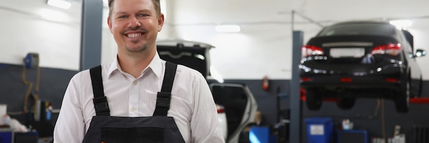 Foto trabalhador de centro de manutenção qualificado sorridente em homem de uniforme posando em fundo de carros no trabalho