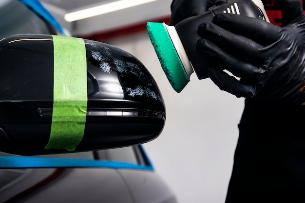 Foto trabalhador de cera de polimento de carros mãos aplicando fita protetora antes de polir polir e polir carro detalhamento de carro homem segura um polidor na mão e polir o carro ferramentas para polir