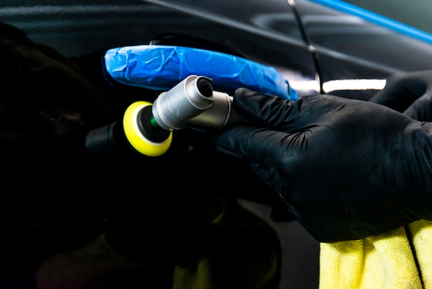 Foto trabalhador de cera de polimento de carros mãos aplicando fita protetora antes de polir polir e polir carro detalhamento de carro homem segura um polidor na mão e polir o carro ferramentas para polir