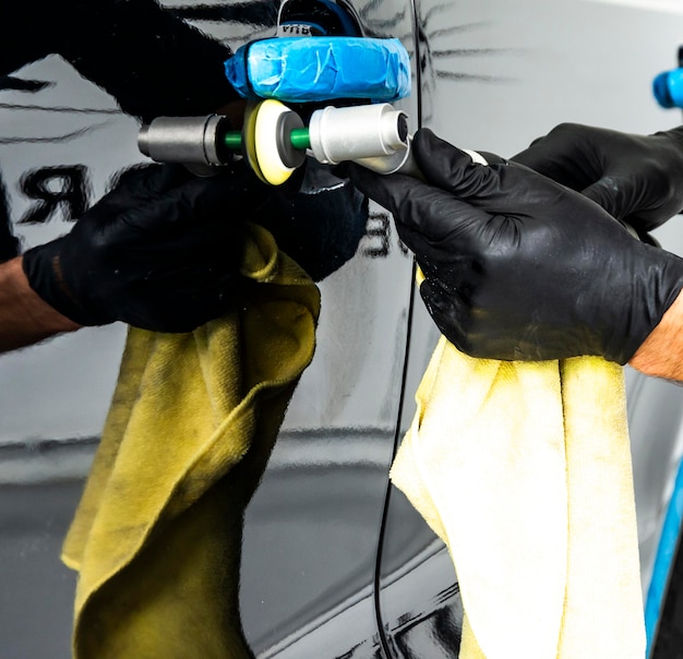 Foto trabalhador de cera de polimento de carros mãos aplicando fita protetora antes de polir polir e polir carro detalhamento de carro homem segura um polidor na mão e polir o carro ferramentas para polir