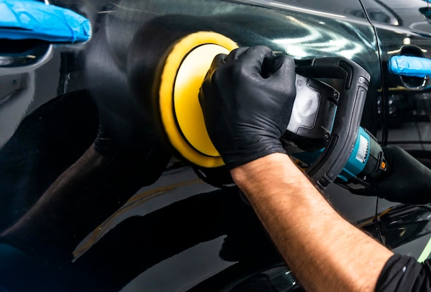 Foto trabalhador de cera de polimento de carros mãos aplicando fita protetora antes de polir polir e polir carro detalhamento de carro homem segura um polidor na mão e polir o carro ferramentas para polir