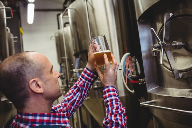 Foto trabalhador de cervejaria, inspecionando cerveja em vidro