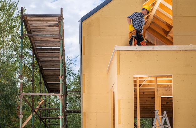 Foto trabalhador de construção e o andaime da recém-construída pequena casa residencial de madeira ao lado da casa