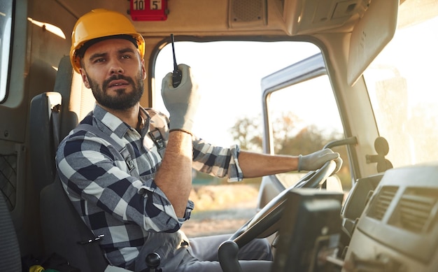 Trabalhador de construção segurando um walkie-talkie de rádio está sentado na cabine do caminhão