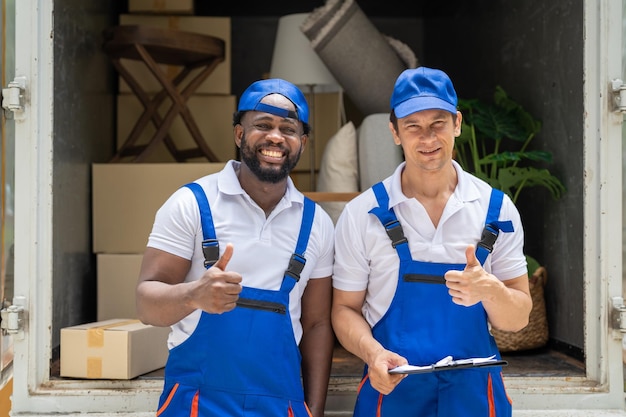 Foto trabalhador de dois homens em uniforme azul aparecendo polegar depois de carregar caixas de papelão do caminhão