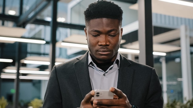 Trabalhador de escritório americano africano jovem sério procurando smartphone na internet escolhendo fazer o pedido