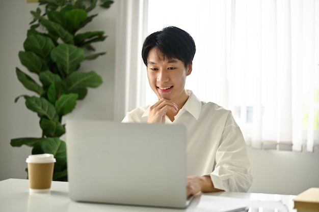 Trabalhador de escritório asiático sorridente usando um laptop e trabalhando em sua mesa no escritório