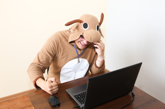 Trabalhador de escritório com fantasia de cosplay de uma vaca. cara de pijama engraçado animal falando ao telefone. paródia sobre o gerente desesperado perto do laptop. burnout ocupacional.