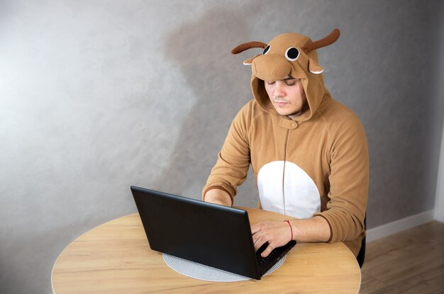 Trabalhador de escritório com fantasia de cosplay de uma vaca. cara de pijama engraçado animal perto do laptop. o homem está trabalhando em casa. trabalho de busca, conceito de desemprego, crise econômica. trabalho remoto.