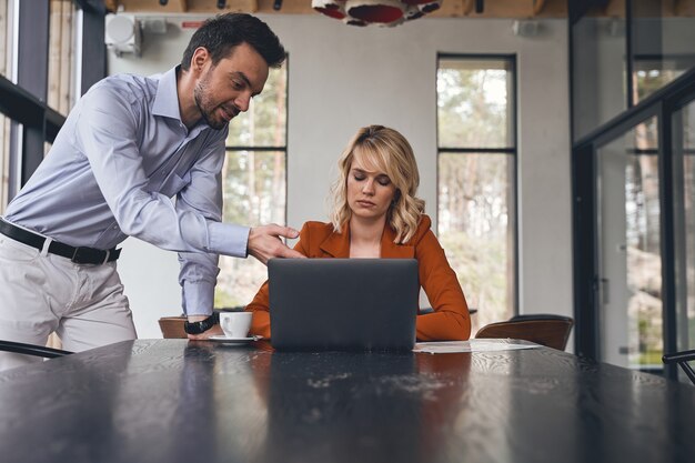 Trabalhador de escritório concentrado apontando para algo na tela do laptop para sua chefe adormecida