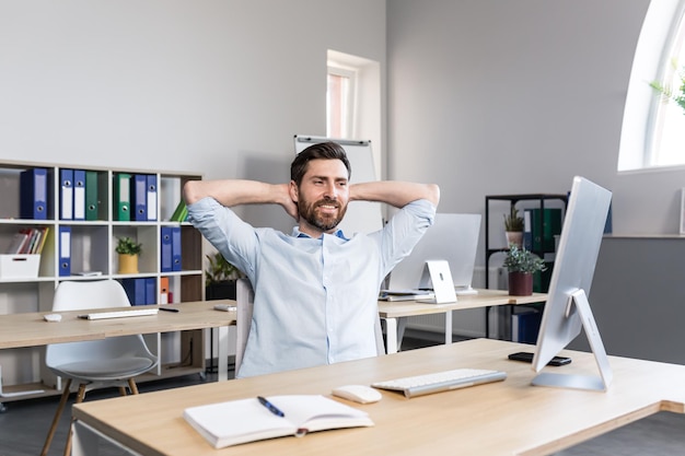 Trabalhador de escritório jovem bonito sentado em uma mesa de computador esticando cansado fazendo uma pausa fazendo exercícios de ioga descansando