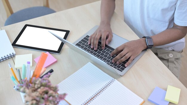 Trabalhador de escritório masculino de tiro recortado usando computador portátil na mesa de madeira