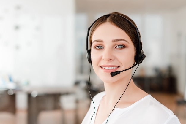 Trabalhador de escritório novo de sorriso com uns auriculares que respondem em um centro de chamadas, mulher que fala com os clientes.