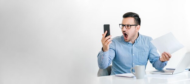 Foto trabalhador de escritório zangado e nervoso de camisa azul gritando olhando para a tela do smartphone