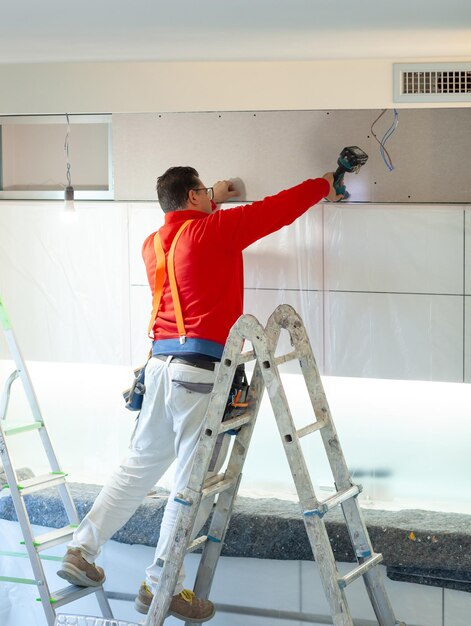 Trabalhador de gesso instala uma parede de gesso nos armários da cozinha