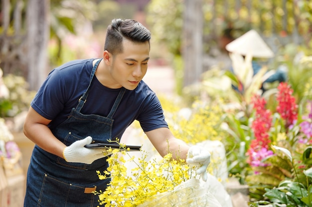 Trabalhador de jardim de infância com tablet digital verificando flores desabrochando de plantas