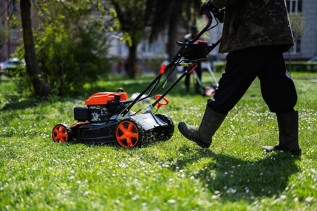 Trabalhador de jardineiro de serviços comunitários usando cortador de grama para cortar grama no parque da cidade