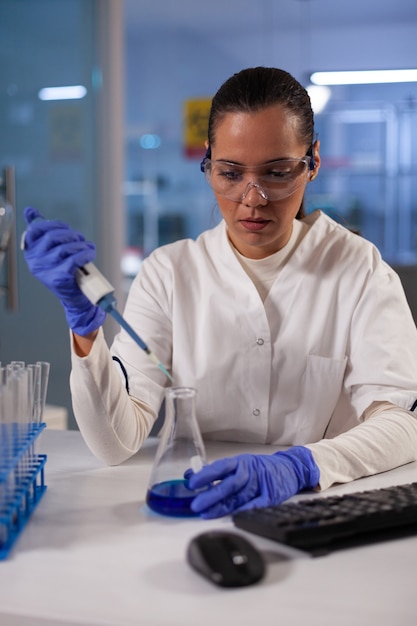 Foto trabalhador de laboratório profissional usando pipeta para recipiente de frasco na indústria médica. mulher de bioquímica científica fazendo testes com tubos para a ocupação de projeto de desenvolvimento médico